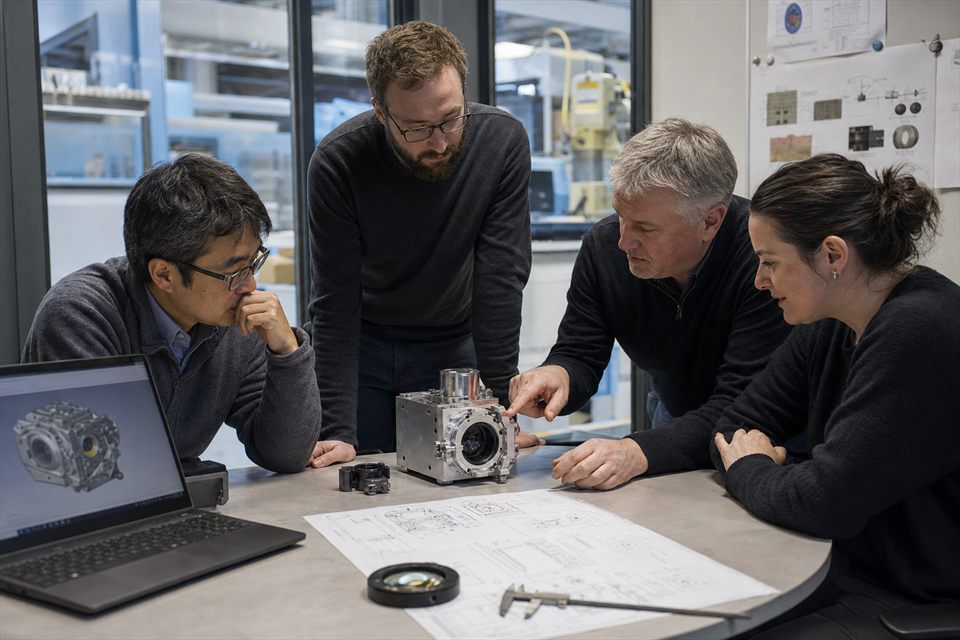 A multidisciplinary engineering group reviewing a physical optical module and drawings